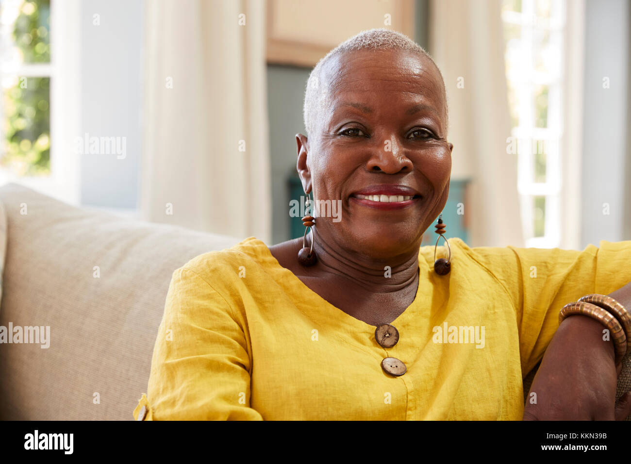 Portrait Of Smiling Senior Woman Sitting On Sofa zu Hause Stockfoto