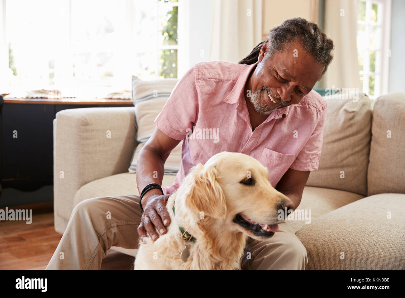 Älterer Mann sitzt auf einem Sofa zu Hause mit Haustier Labrador Hund Stockfoto