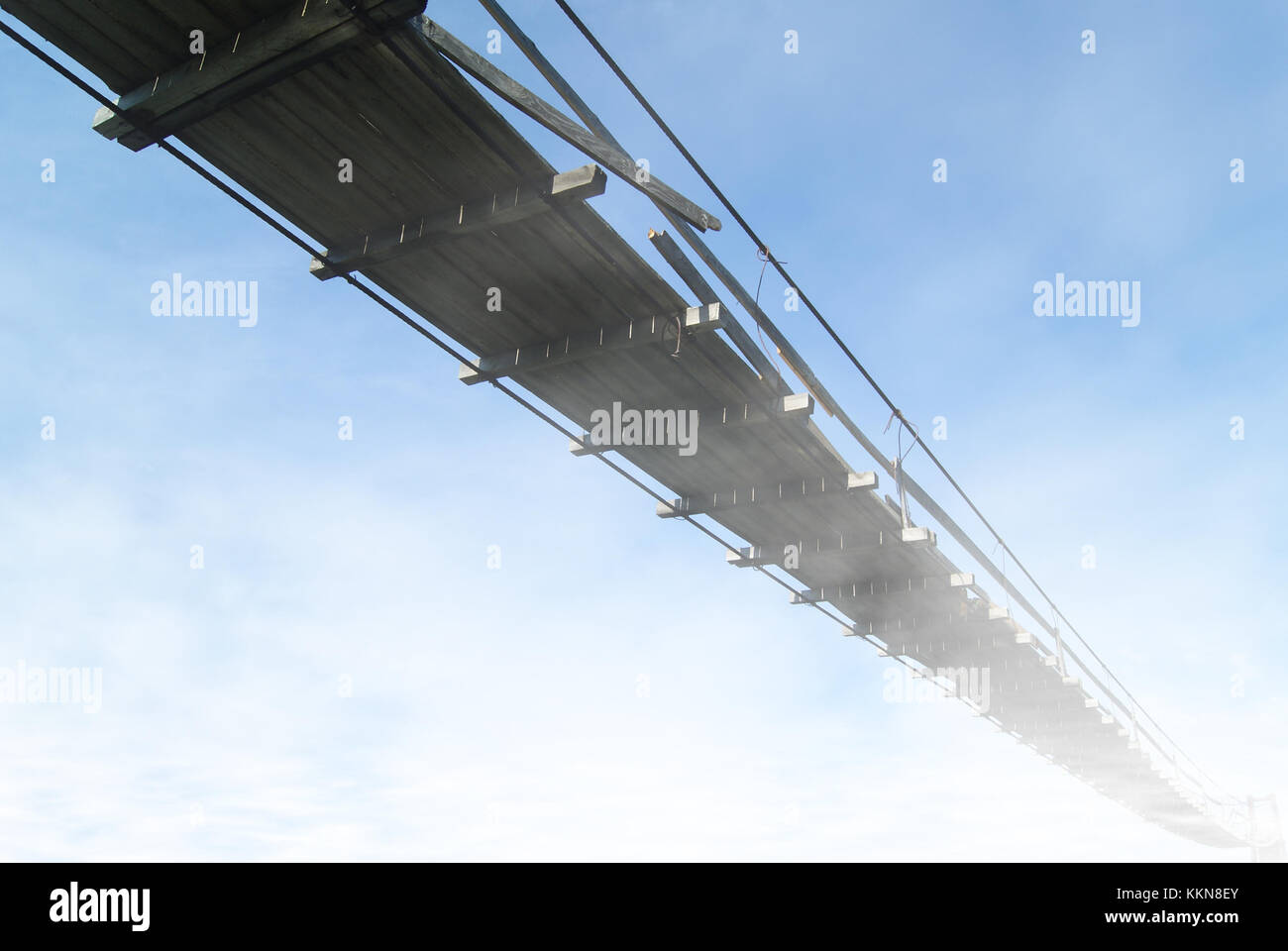 Blick von unten auf eine alte hölzerne Hängebrücke gegen einen Himmel verstecken sich in Wolken in Sicht Stockfoto