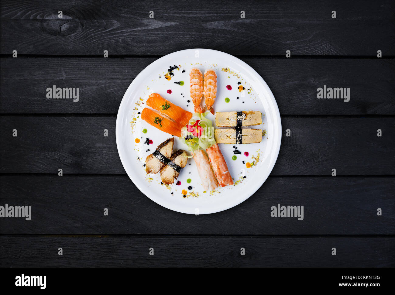 Sashimi auf eine weiße, runde Platte, mit kleinen Blumen, japanisches Essen, Ansicht von oben eingerichtet. schwarz Holz- Hintergrund Stockfoto