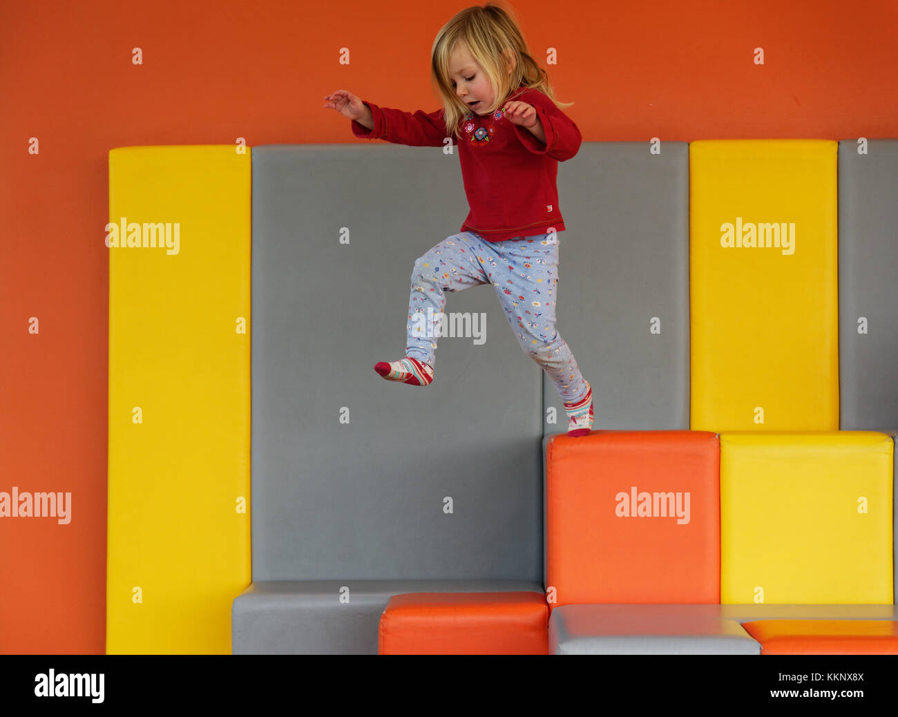 Ein kleines Mädchen (3 Jahre alt) das Springen in einem gepolsterten Spielbereich Stockfoto