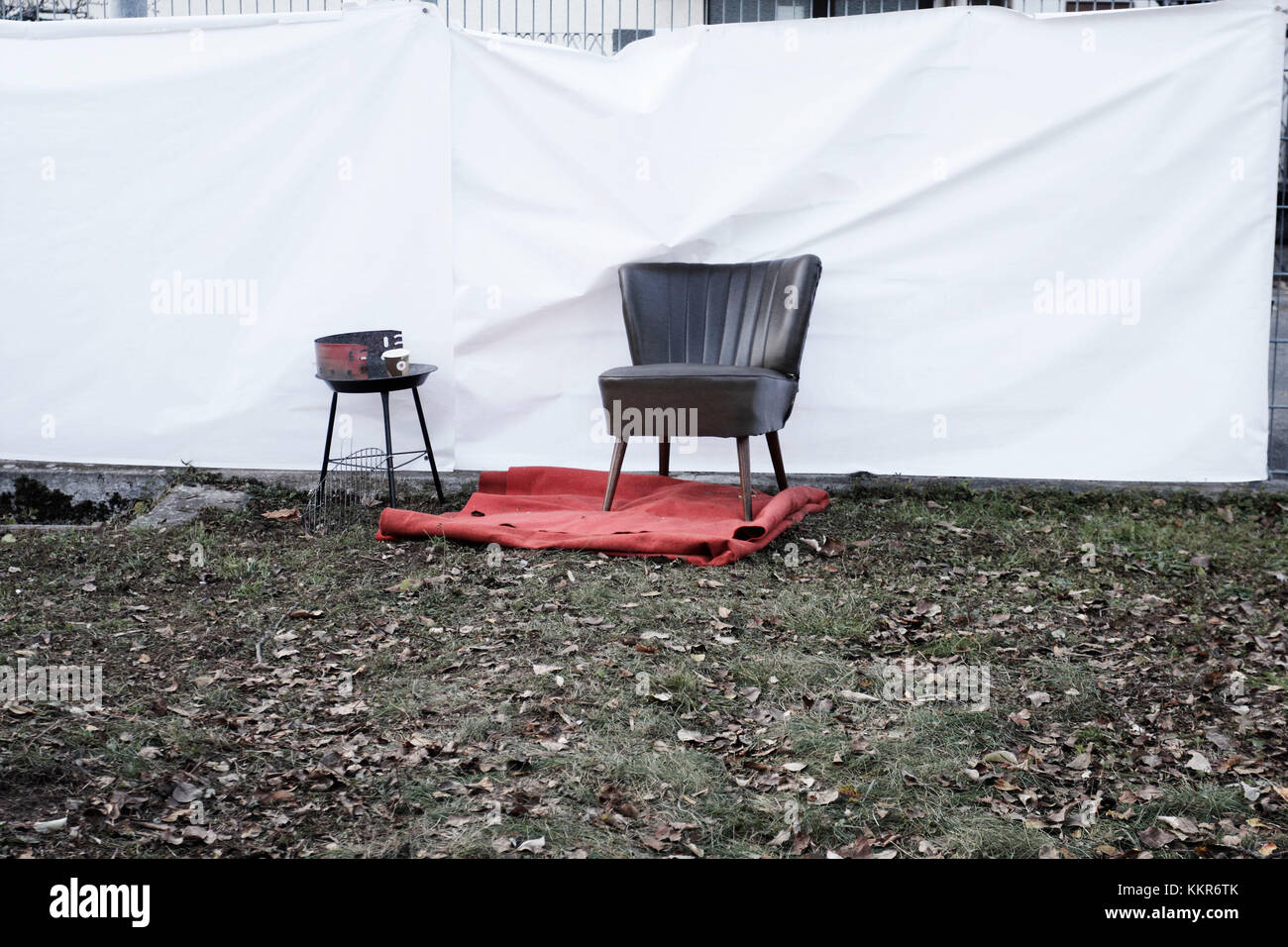 Alten, schwarzen Sessel auf dem roten Teppich und Grill vor dem Zaun mit weißem Kunststoff Blatt Stockfoto