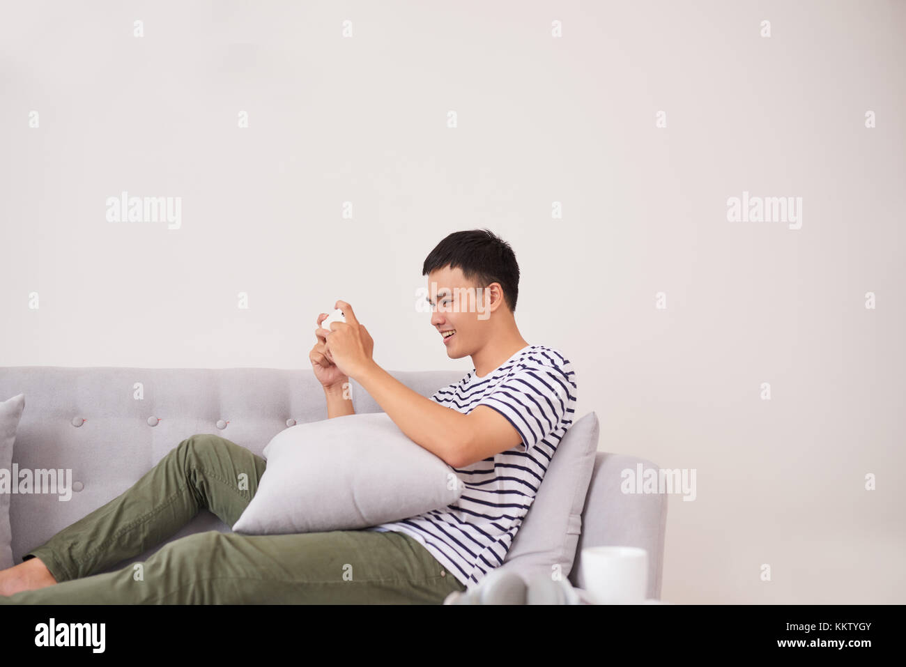 Jungen asiatischen Mann sitzt auf einem Sofa und Spielen am Telefon zu Hause Stockfoto