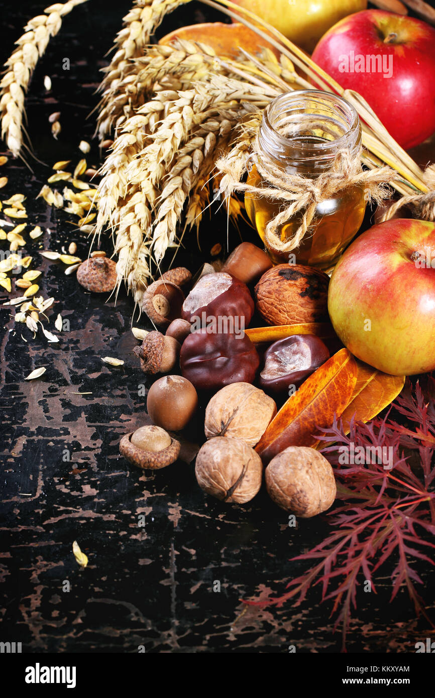 Glas Glas Honig mit Äpfeln, Ähren, Kastanien und Nüssen über schwarzen Holztisch Stockfoto