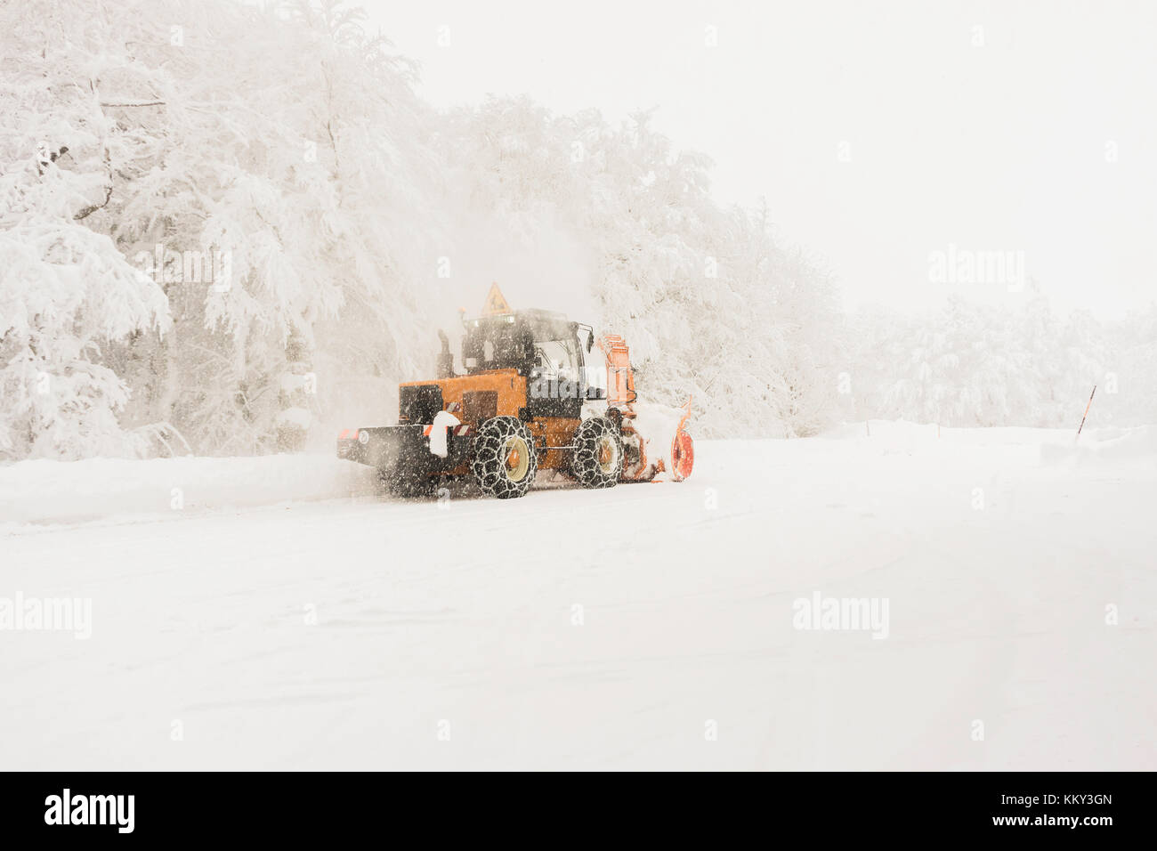 Ein pistenfahrzeug arbeiten, während es schneit, um die Straße für den Verkehr zu erhalten; Vogesen im Winter, Frankreich. Stockfoto