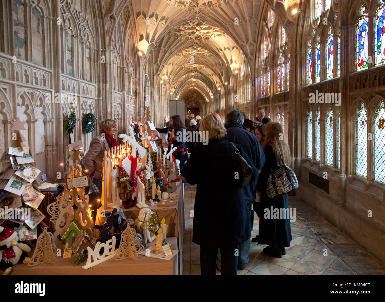 Weihnachtseinkäufer schlendern durch festliche Marktstände in den kunstvollen und historischen Kreuzgängen der Kathedrale von Gloucester in Großbritannien Stockfoto