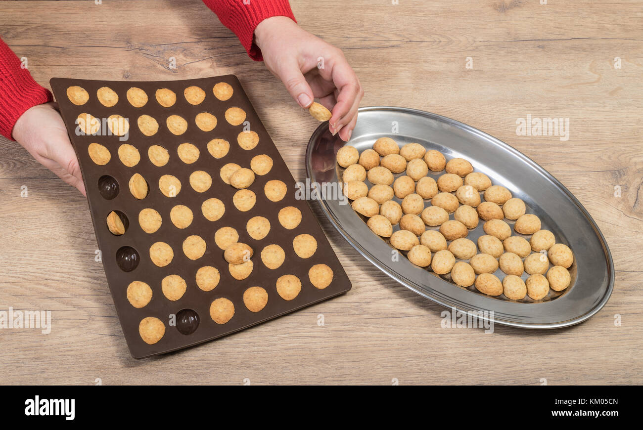 Die von Weihnachten Nüsse aus Mürbeteig verkneten. Hände, silikonform und Salver mit frisch gebackenen Cookies auf Holz Hintergrund. Stockfoto