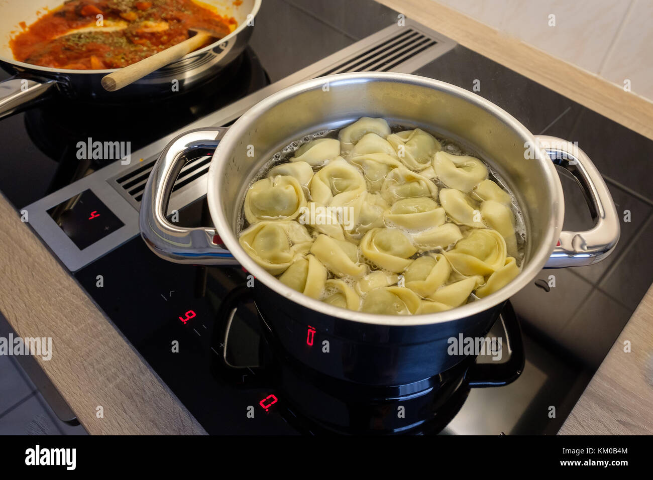 Topf mit Tortelling und Pan mit Tomatensauce auf einem Kochfeld Stockfoto