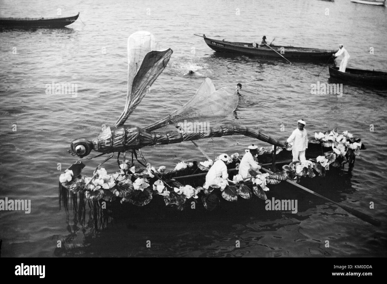 Schwarz-weiß-Bild um des späten 19. oder frühen 20. Jahrhundert, ein wachsendes Boot in einem Festival, mit einem riesigen Kunstvollen Dragonfly Modell, fast die Länge des Bootes. Boot ist auch mit Blumen verziert und hat zwei Männer rudern und einem anderen Mann auch auf dem Boot. Stockfoto