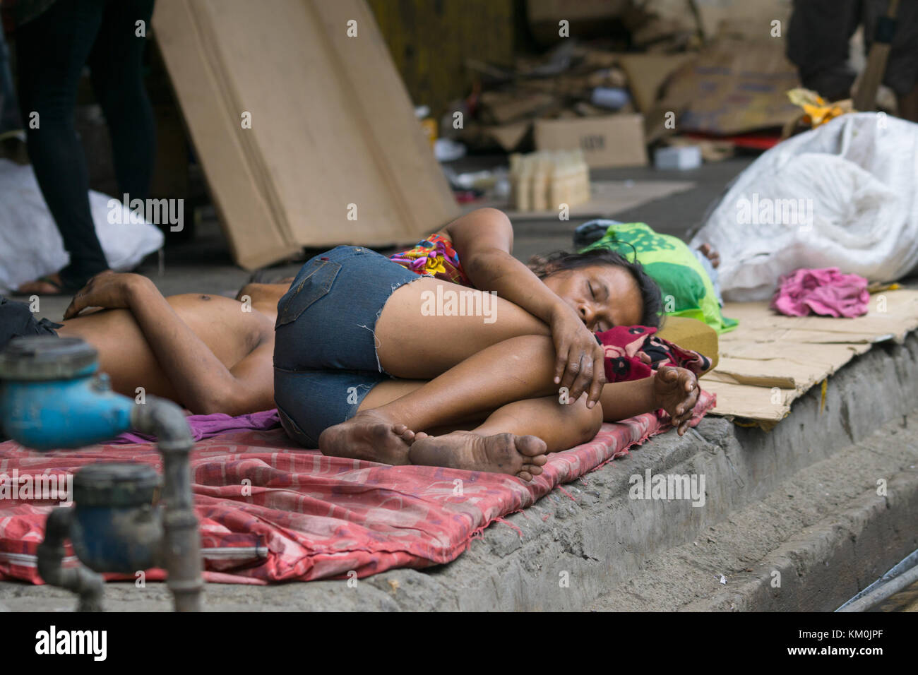 Eine Frau mit einem Mann schläft auf einem Bürgersteig während des Tages in Cebu City, Philippinen Stockfoto