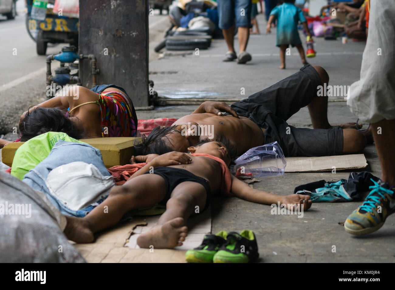 Ein Kind mit einem Mann & Frauen schlafen auf dem Bürgersteig während des Tages in Cebu City, Philippinen Stockfoto