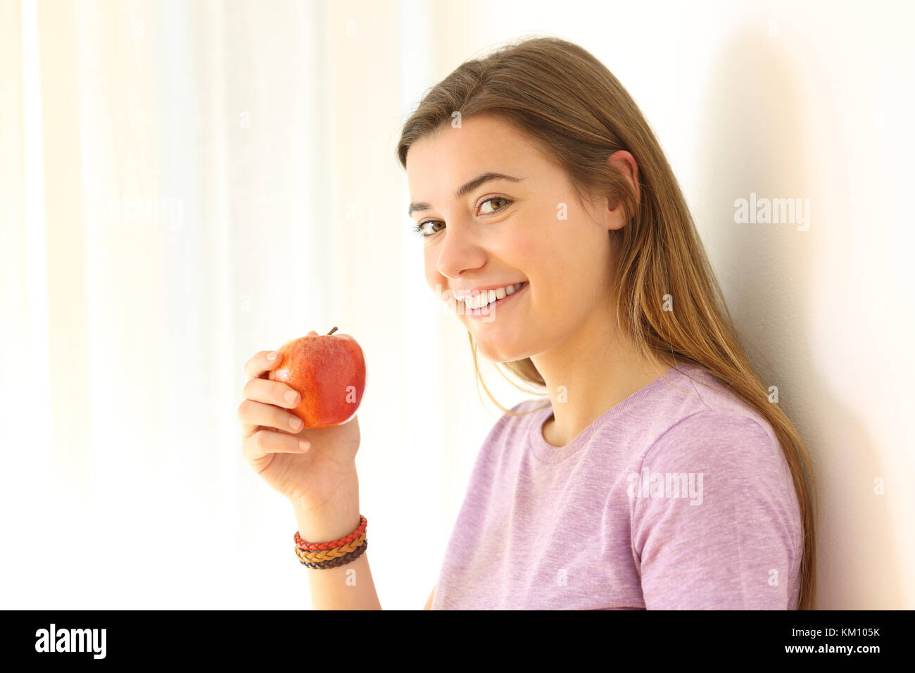Portrait Of Happy Teen mit einem Apfel und sie lehnte sich an eine Wand in einem Haus innen Stockfoto