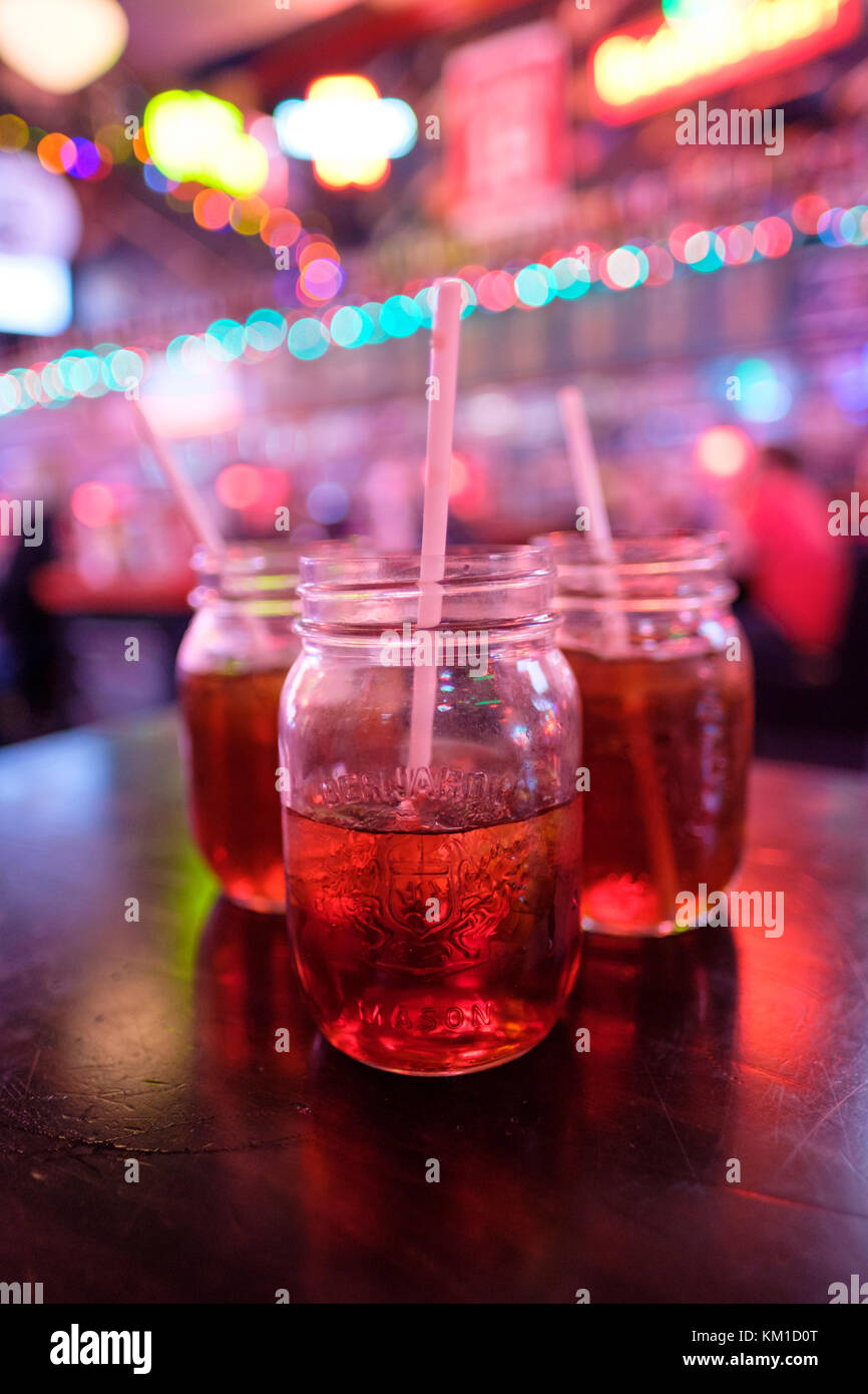 Obst Getränke, Säfte, Getränke in Mason Gläser auf einen hölzernen Tisch in einer Bar mit aus Menschen und Neonlicht im Hintergrund, festliche Stimmung. Stockfoto