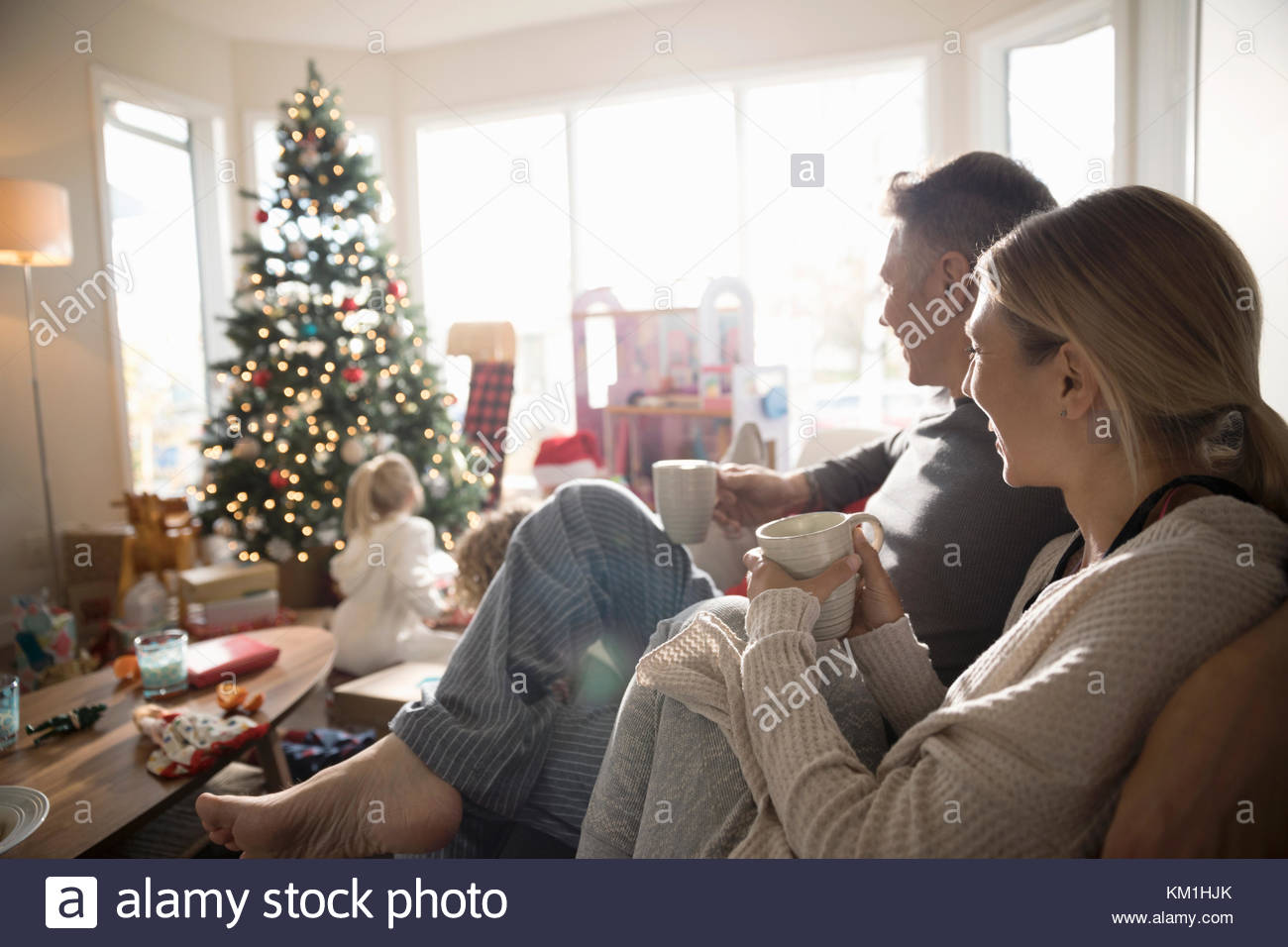 Eltern Kaffee trinken, gerade Töchter öffnung Weihnachtsgeschenke im Wohnzimmer Stockfoto