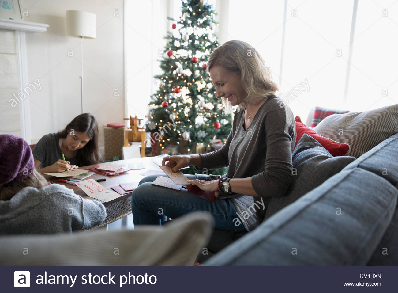 Lächelnde Mutter und Töchter zu Weihnachten Karten in der Nähe von Weihnachten Baum im Wohnzimmer Stockfoto