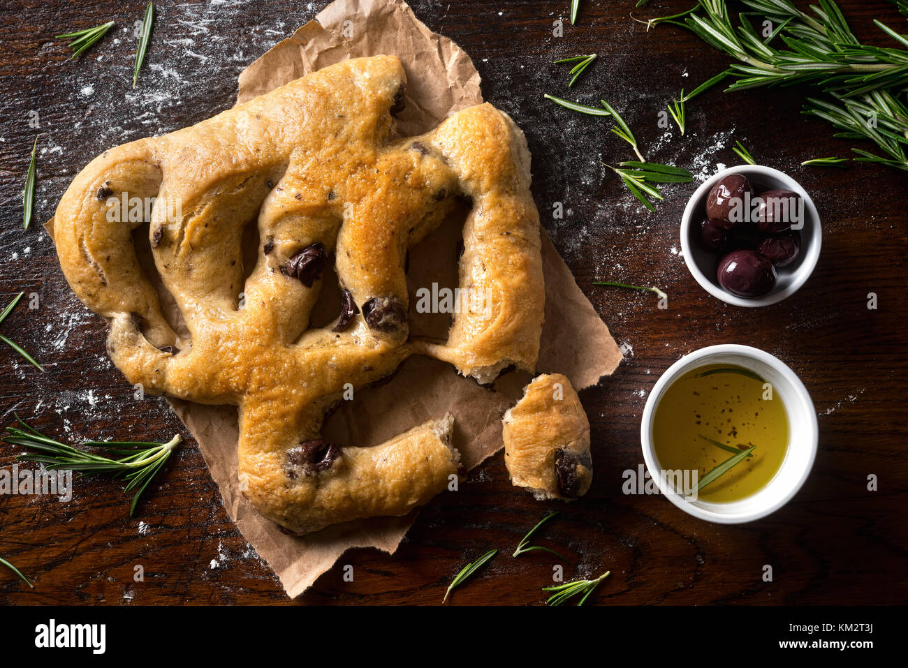 Eine köstliche Focaccia-brot mit schwarzen Oliven und Rosmarin auf einem rustikalen Tischplatte. Stockfoto