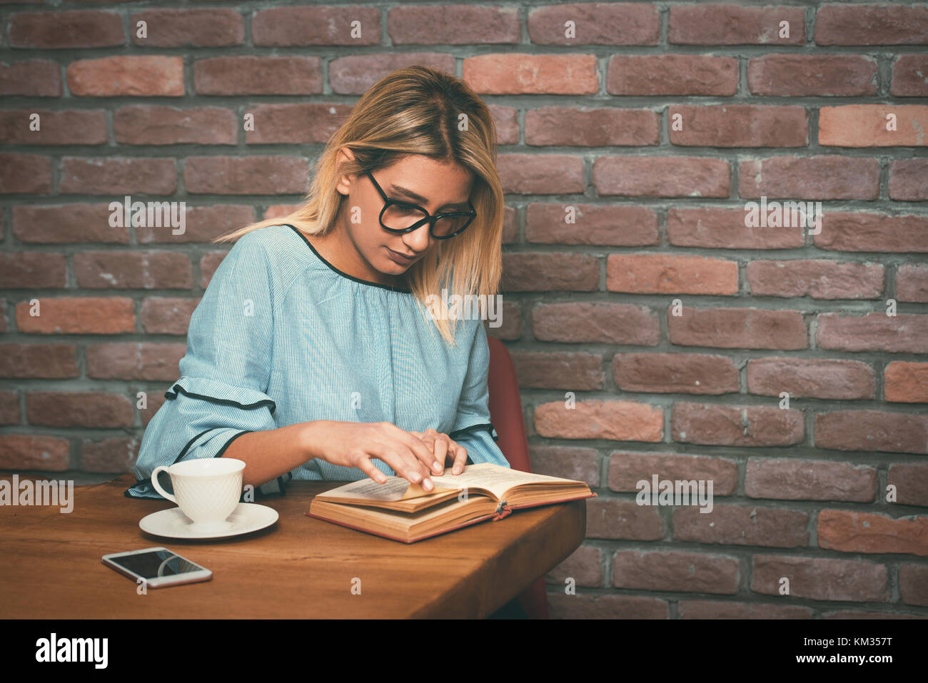 Junge blonde Frau sitzt viel Spaß beim Lesen Buch im Cafe. vintage Filter abgeschwächt. Stockfoto