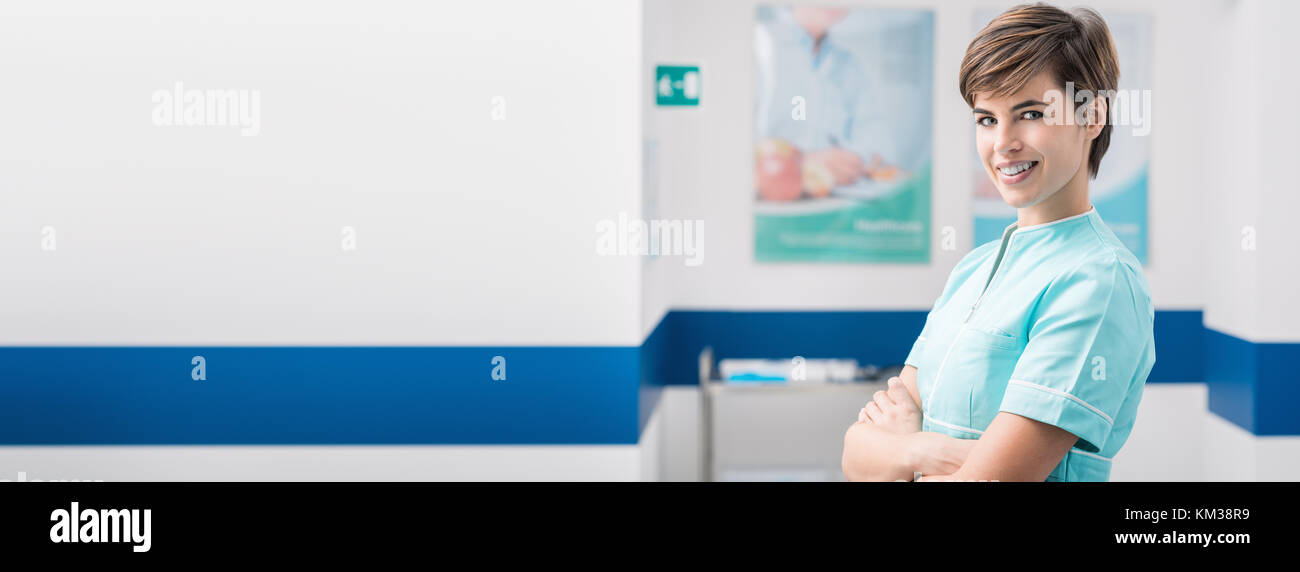 Selbstbewussten jungen Frau Krankenschwester posiert im Krankenhaus gang und lächelnd an Kamera, Healthcare Professionals banner Stockfoto