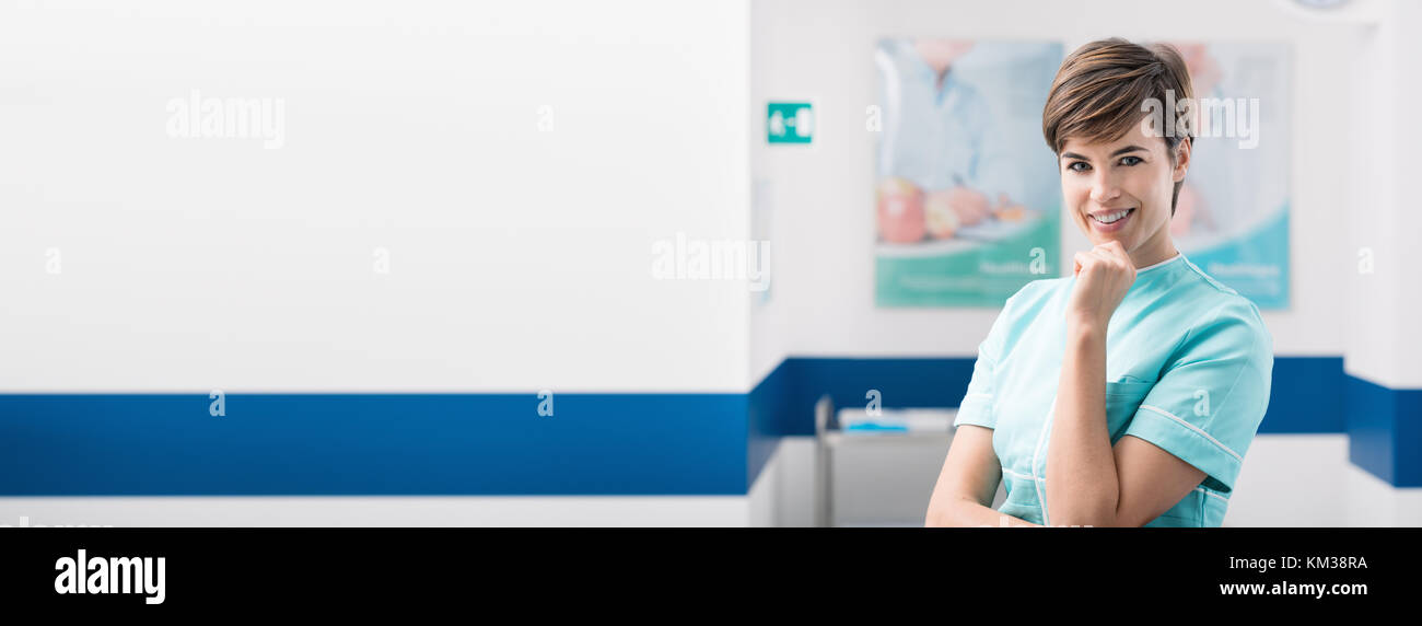 Selbstbewussten jungen Frau Krankenschwester posiert im Krankenhaus gang und lächelnd an Kamera, Healthcare Professionals banner Stockfoto