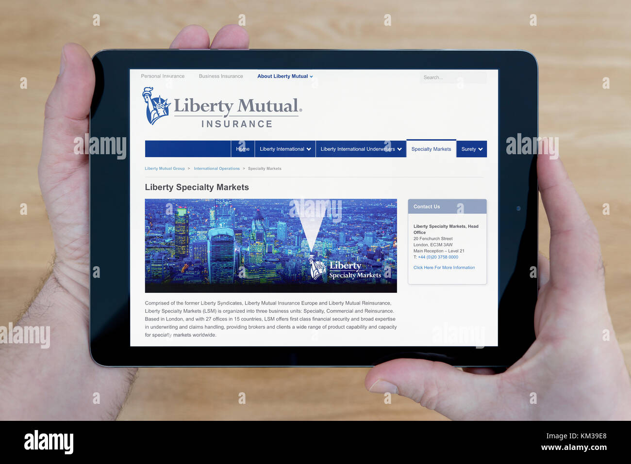Ein Mann schaut auf die Liberty Mutual Insurance Website auf seinem iPad tablet device, Schuß gegen einen hölzernen Tisch top Hintergrund (nur redaktionelle Nutzung) Stockfoto