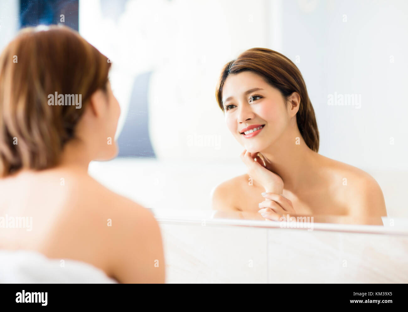 Junge Frau auf der Suche nach Reflexion im Spiegel im Badezimmer Stockfoto