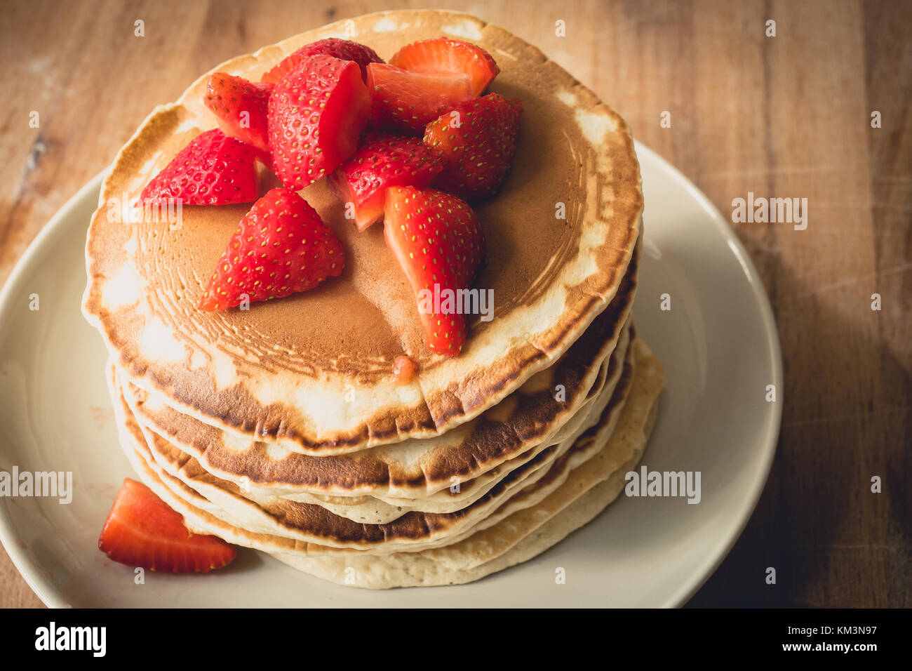 Ein Stapel von hausgemachte Pfannkuchen auf einer weißen Platte mit geschnittenen Erdbeeren auf die Oberseite. Querformat. Stockfoto