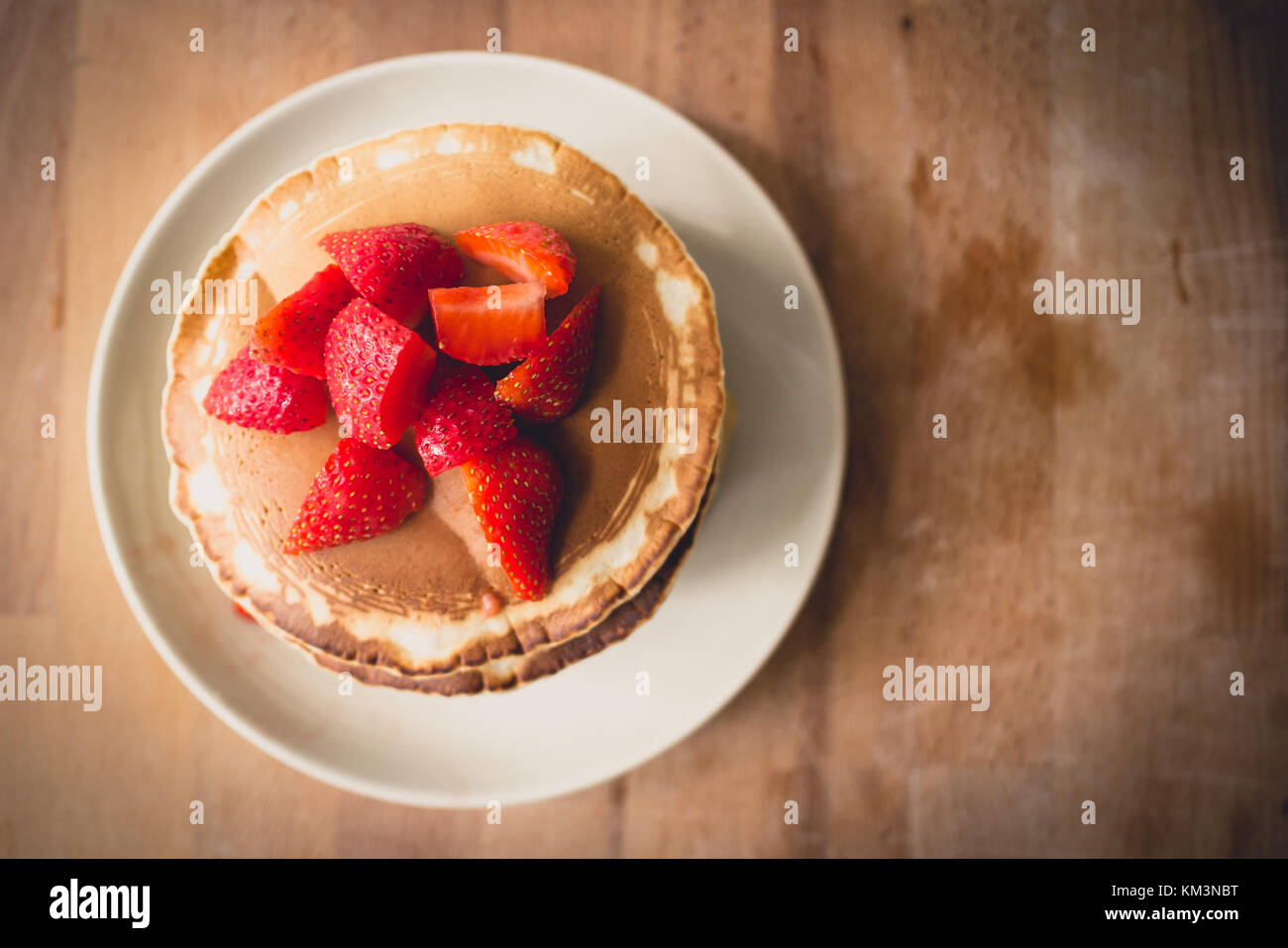 Nahaufnahme von einem Stapel von hausgemachte Pfannkuchen auf einer weißen Platte mit geschnittenen Erdbeeren und Ahornsirup. Stockfoto