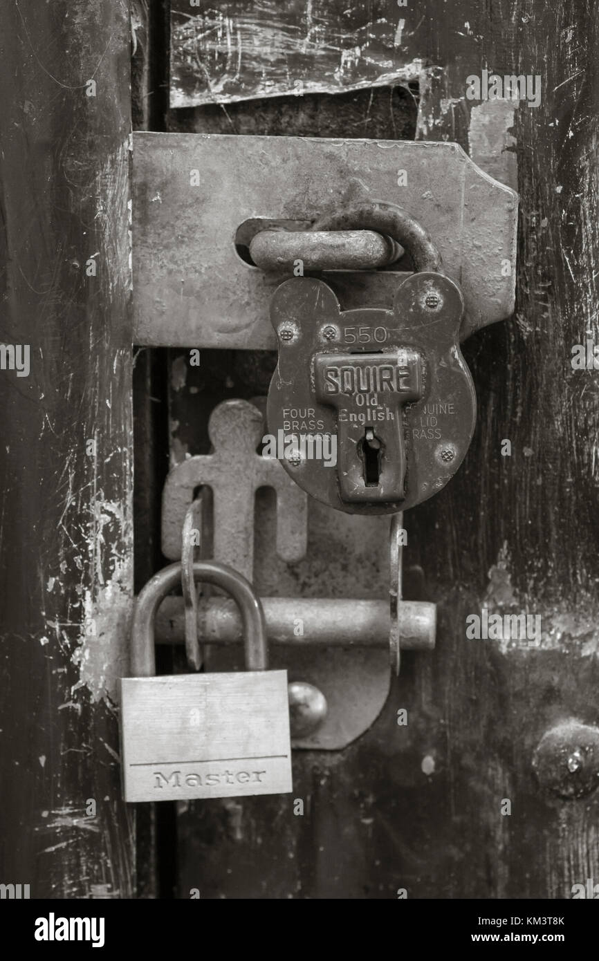 Schwarz-Weiß-Bild von zwei Vorhängeschlössern auf rauem Außeneingang. Für gesperrte Daten, Daten- und E-Mail-Sicherheit, Denial-of-Service, sperren Sie sie, Covid-Sperre. Stockfoto