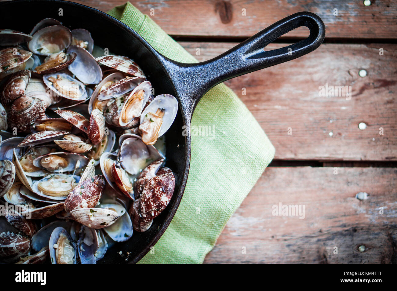 Gusseisen Skillet von köstlichen frischen Dampfgarer Muscheln mit Knoblauch und Basilikum auf rustikalen hölzernen Hintergrund Stockfoto