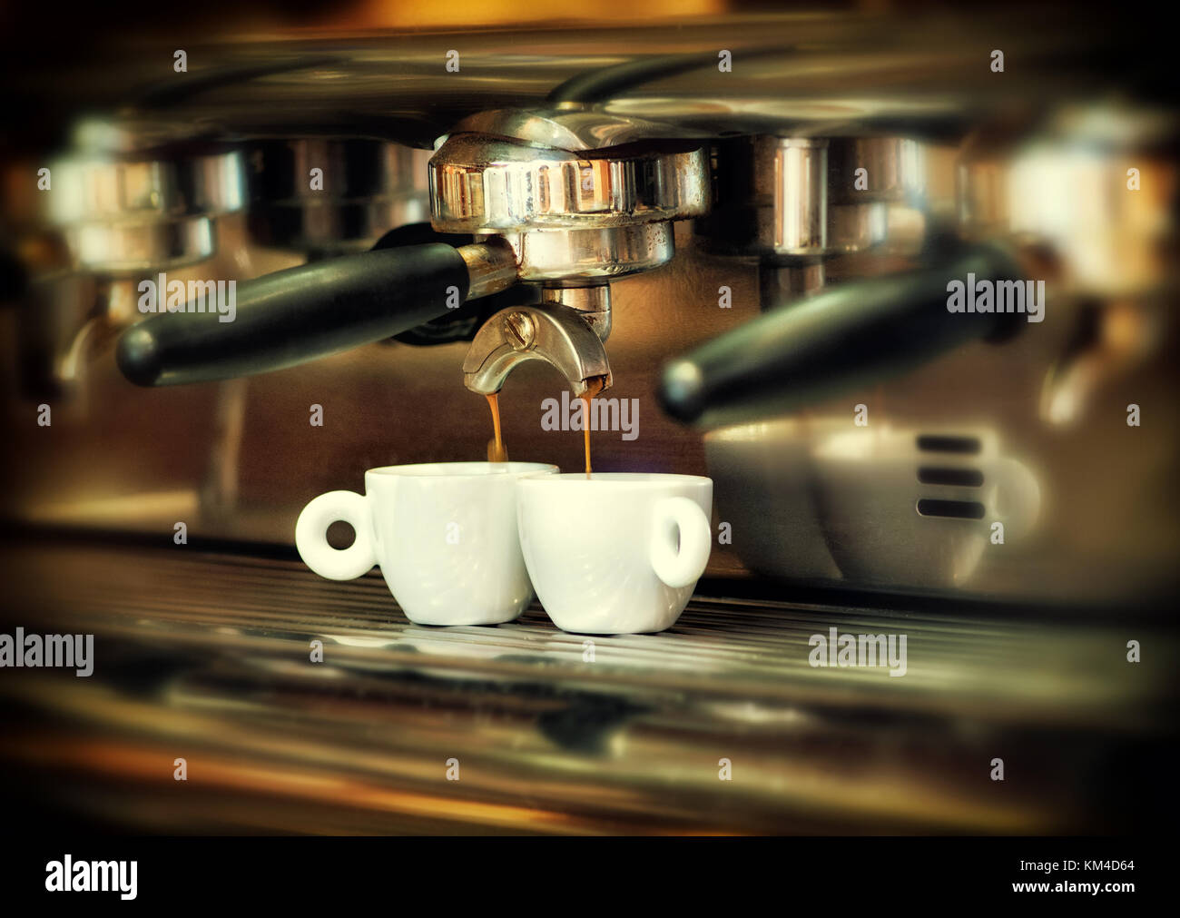 Kaffeemaschine mit schwarzem Griff gießt heißen Kaffee in zwei weiße keramische Tassen. Close-up von der Seite gesehen Stockfoto