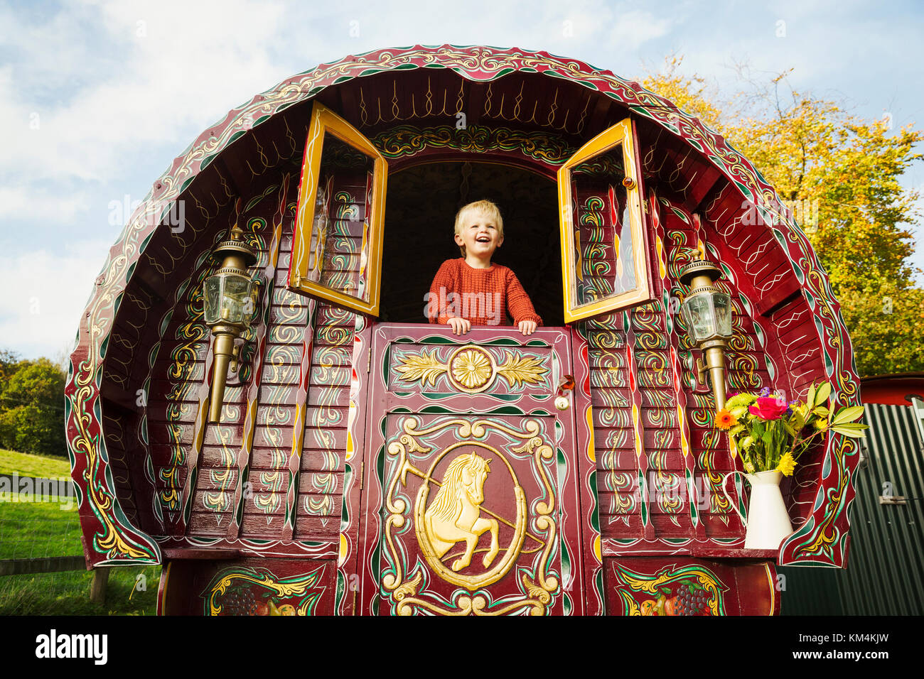 Ein Junge lehnte sich aus dem geöffneten Fensterläden an der Rückseite eines Bogen Gypsy Caravan. Stockfoto