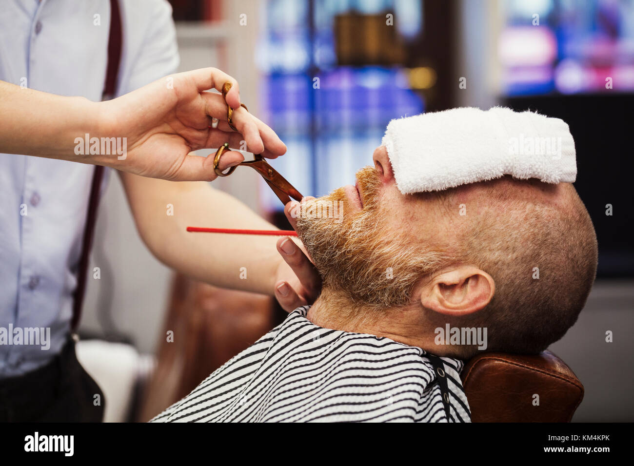 Ein Kunde in der Friseur Stuhl sitzen, mit einem warmen Handtuch auf sein Gesicht, und ein Friseur Schneiden von Bart. Stockfoto