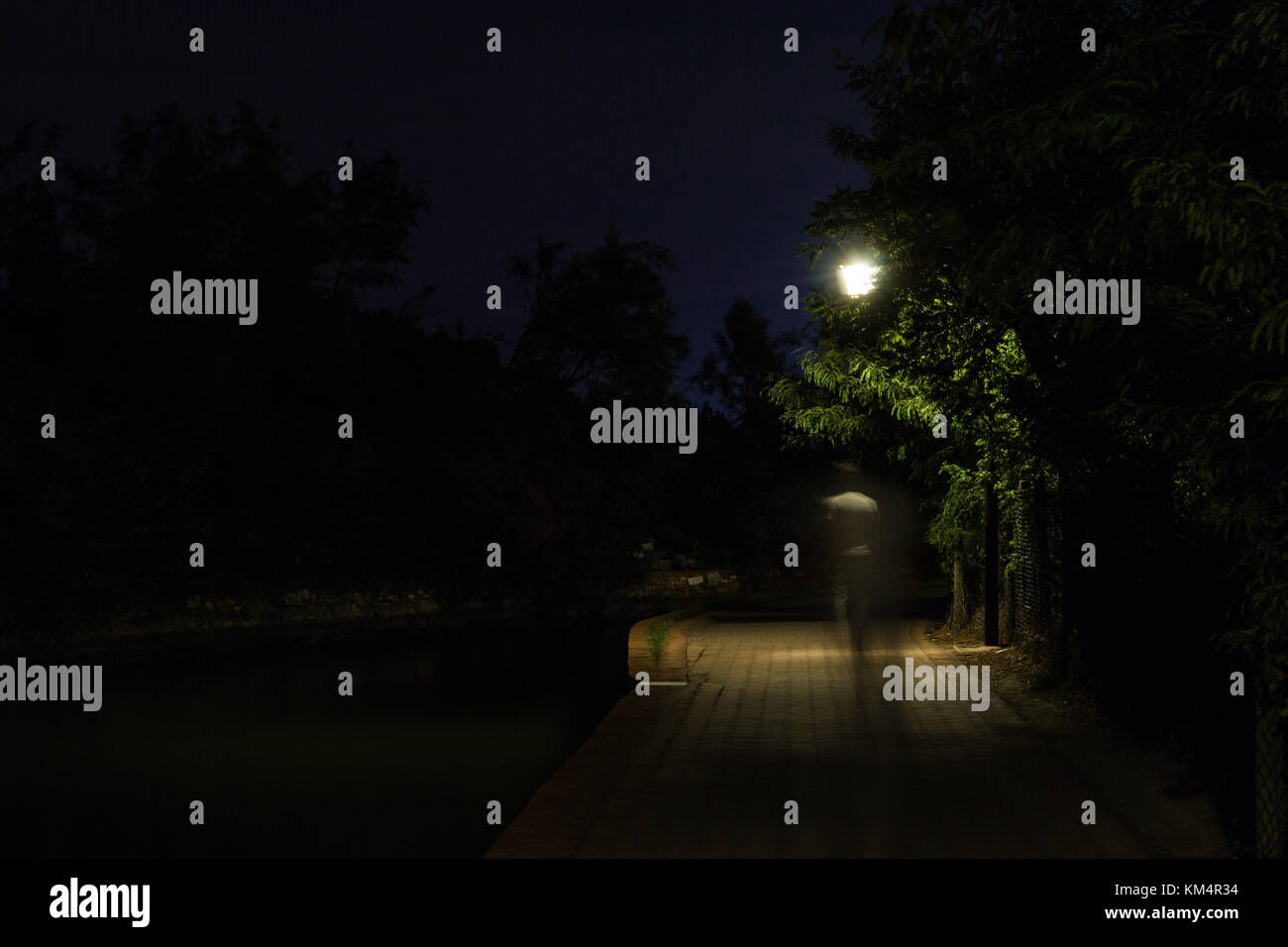 Double Exposure Nacht Szene von Person zu Fuß dunkle Straße mit Straßenlaternen beleuchtet. Die Zurückweichenden männlichen Silhouetten auf dem Weg in den Park. Stockfoto