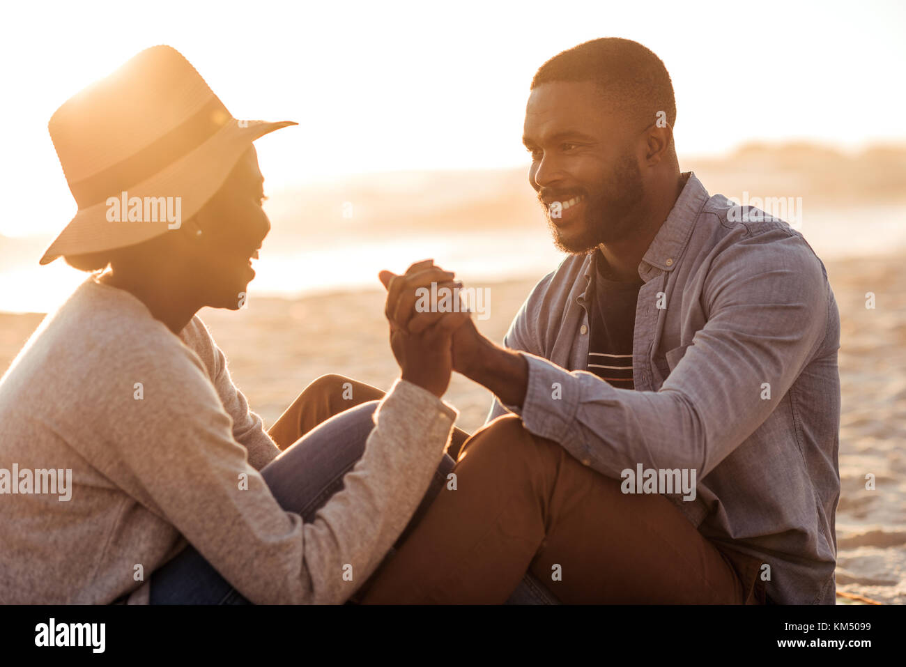 Junge afrikanische Paar zusammen sitzen auf einem Strand bei Sonnenuntergang Stockfoto