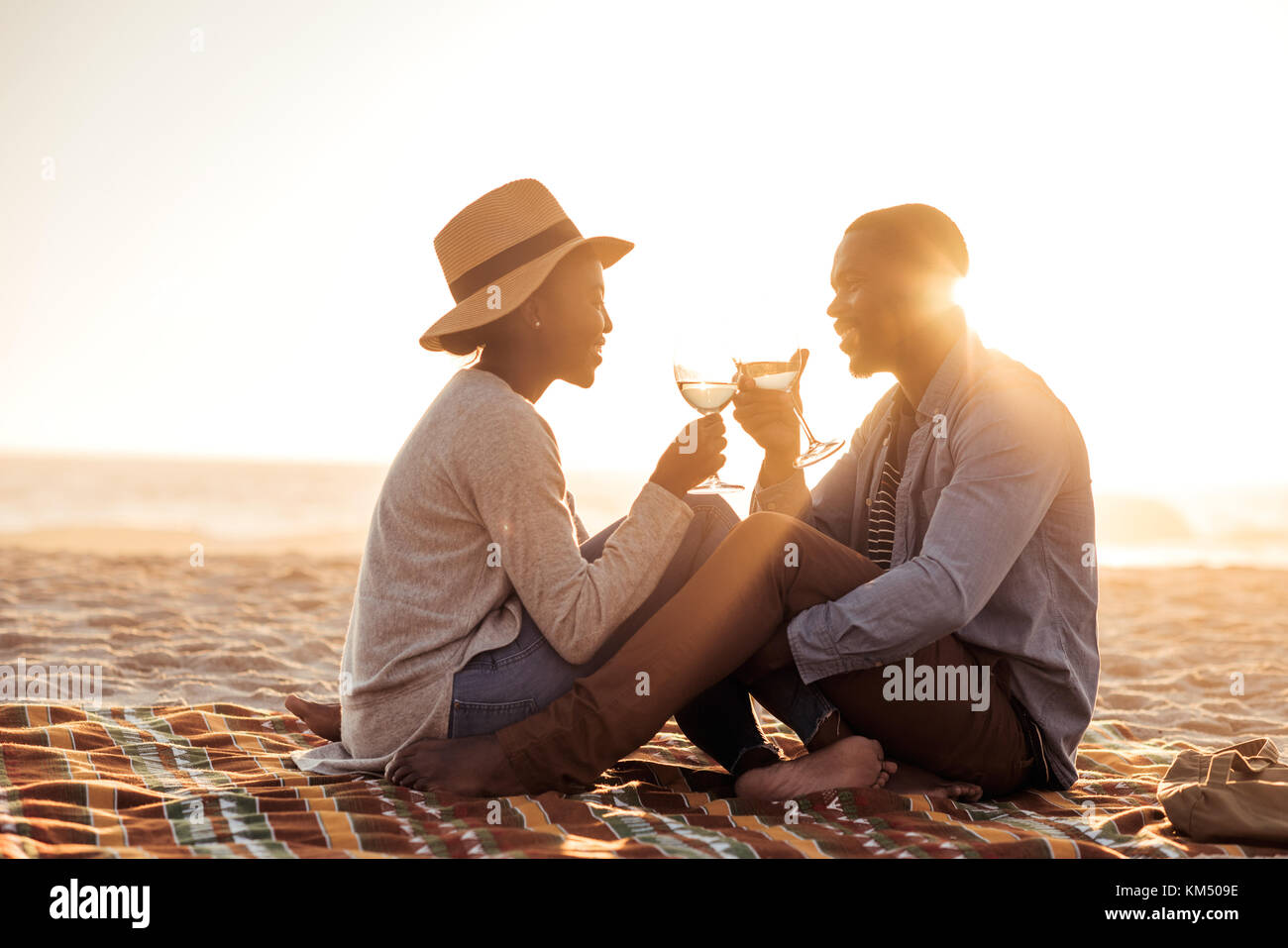 Junge afrikanische Paar Wein trinken und am Strand bei Sonnenuntergang Stockfoto