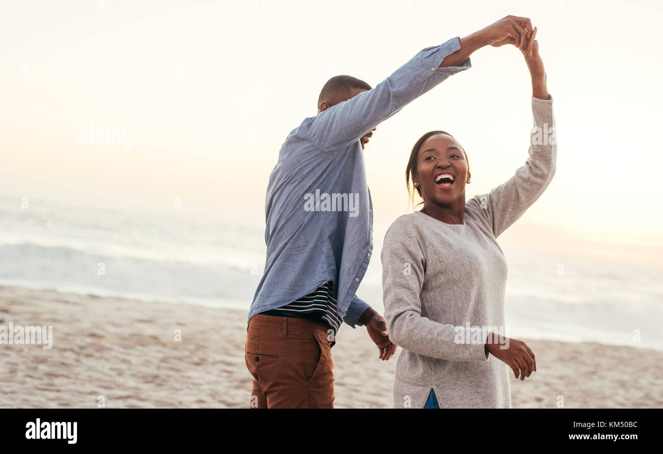 Lachend afrikanischen Paar tanzen zusammen am Strand bei Sonnenuntergang Stockfoto