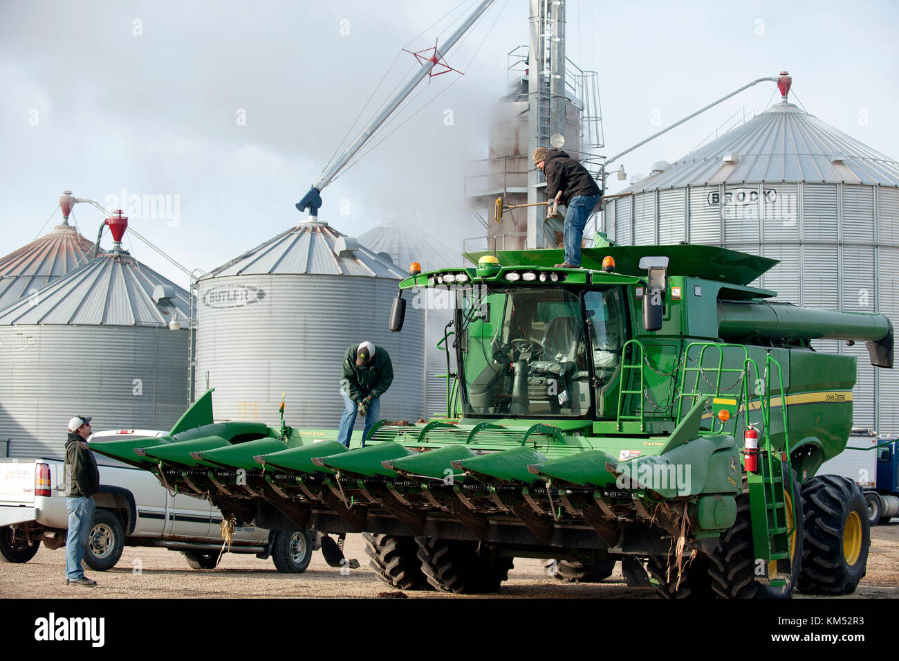 Bauer und Arbeiter SAUBER EIN JOHN DEERE Mähdrescher vor der Überschrift heraus ZUR ERNTE VON MAIS AUF EINEM BAUERNHOF in Utica, Minnesota. Stockfoto