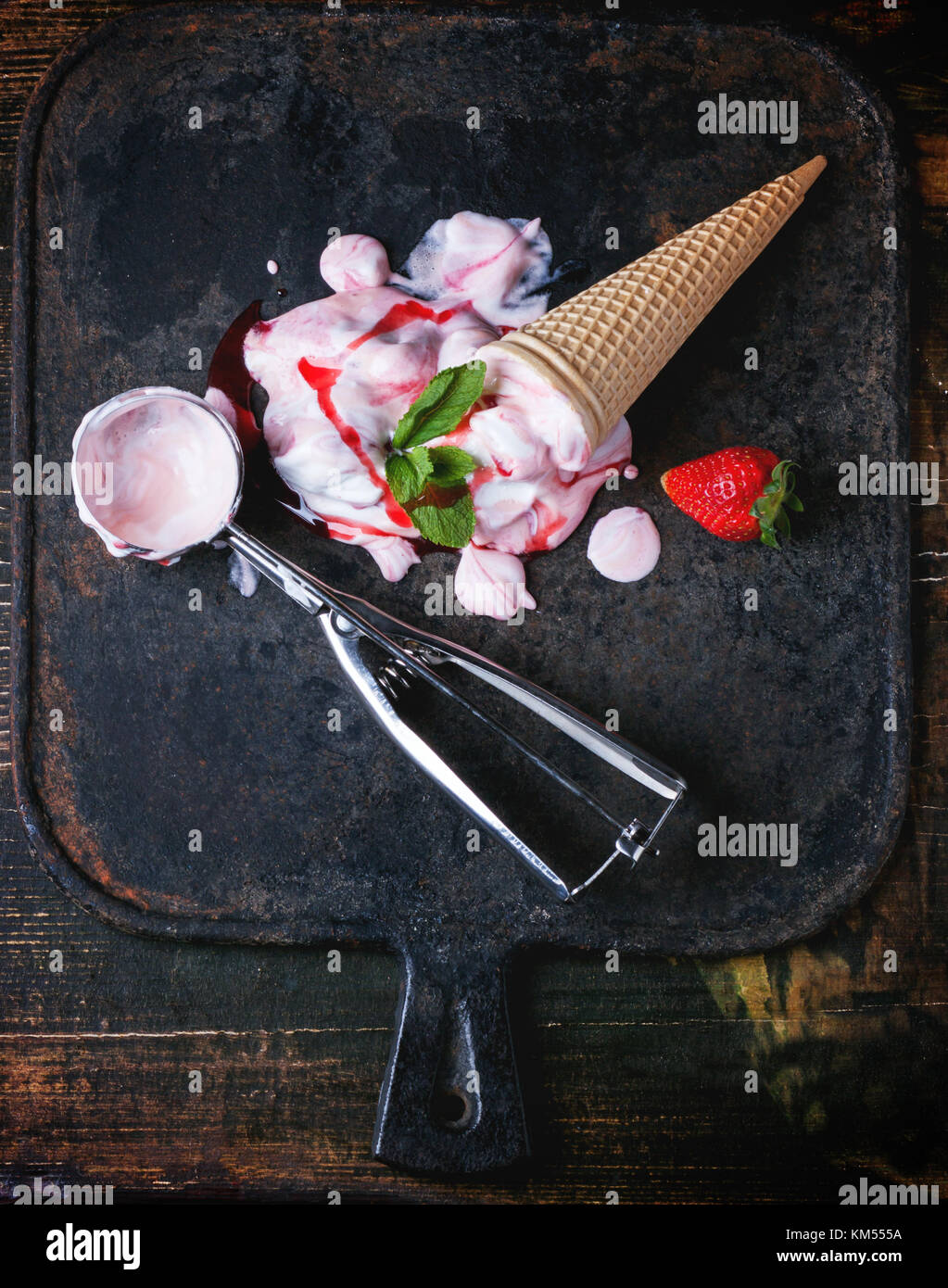 Wafer Kegel mit Erdbeereis mit frischen Erdbeeren, Minze und Metalllöffel über schwarzen gusseisernen Board. Ansicht von oben. Stockfoto