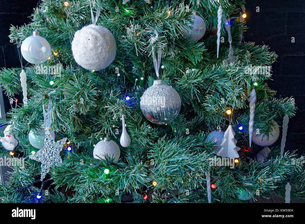 Nahaufnahme der weißen Kugeln und Dekorationen mit bunten Lichtern auf einem Xmas Tree Stockfoto