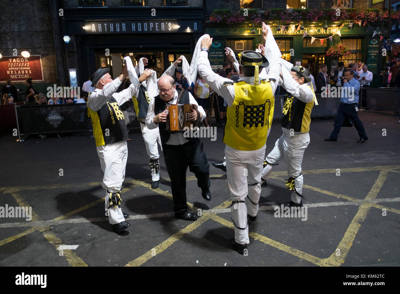 Morris Dancers vom Westminster Morris Men, die Durchführung von außerhalb in den Borough Market in einem Sommer Abend bei Menschen für einen Drink am Abend sehen Sie in London, Vereinigtes Königreich. Die westminster Morris Men mit Stöcken durchführen. Morris Dance ist eine Form des Englischen Volkstanz in der Regel mit Musik begleitet. es auf rhythmische Intensivierung und die Ausführung von Choreografierten Abbildungen, die durch eine Gruppe von Tänzern, die in der Regel tragende Bell Pads auf ihre Schienbeine stützt. Der älteste bekannte und erhaltene Englisch schriftliche Erwähnung von Morris Dance ist auf 1448 datiert. Stockfoto