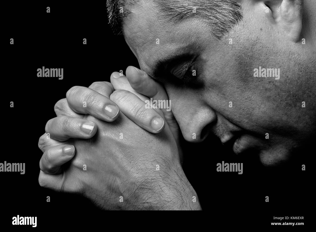 Nahaufnahme der Gläubigen reifer Mann betende Hände gefaltet Gott verehren, Kopf und Augen in religiösen schwarzen Hintergrund Religion Porträt Christian geschlossen Stockfoto