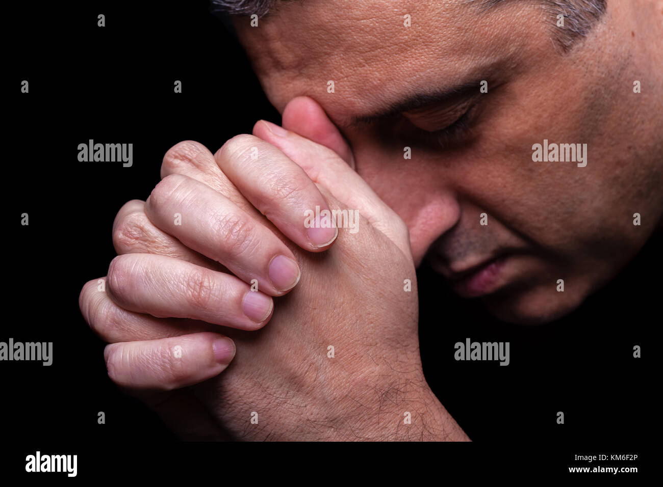 Nahaufnahme der Gläubigen reifer Mann betende Hände gefaltet Gott verehren, Kopf und Augen in religiösen schwarzen Hintergrund Religion Porträt Christian geschlossen Stockfoto