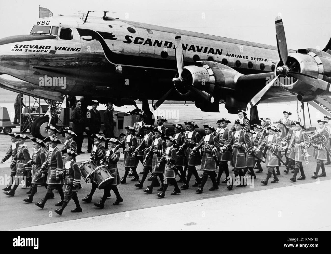 Diese Abbildung zeigt das SAS DC 4-Flugzeug, das durch die DFY-Registrierung Sigvard Viking OY identifiziert wurde, am Boden am Flughafen. Eine Parade von Militärmusikern begleitet die Szene. Das Flugzeug war früher als Passad SE BBC bekannt und war von 1948 bis 1954 aktiv. Stockfoto
