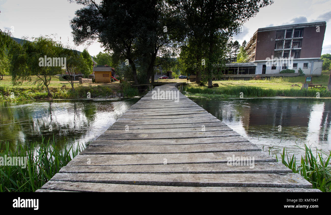 Ein Holzsteg Überquerung des Flusses Gacka auf das neue Hotel gacka mit der aufgegebenen alten Hotel auf der rechten Seite. Stockfoto
