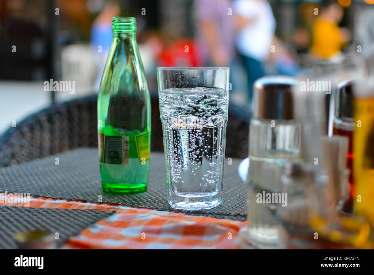 Ein Glas Wasser mit Kohlensäure mit Blasen und Nebel steigende sitzt neben einem leeren grünen Flasche in einem Straßencafé Stockfoto