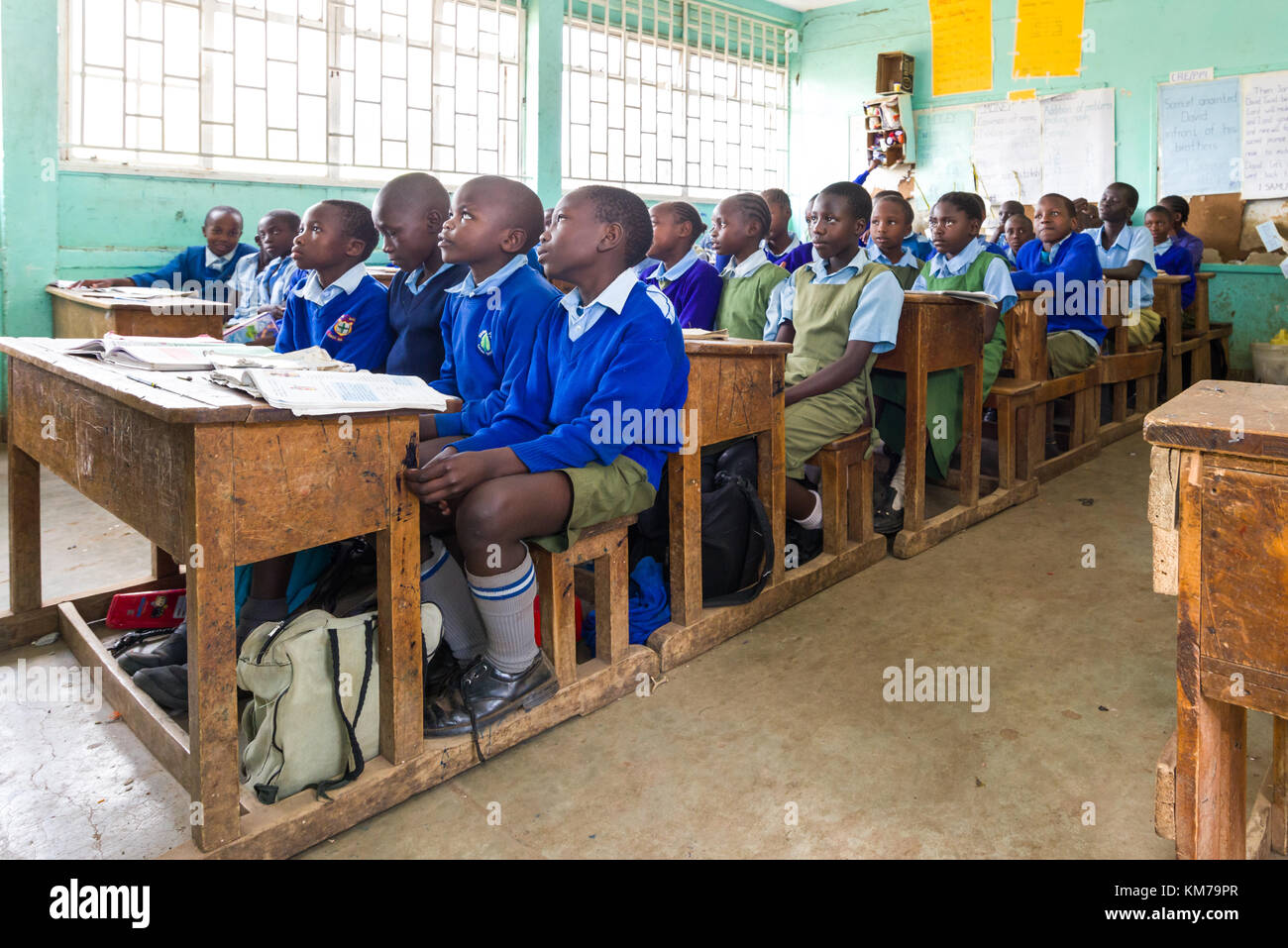 Schulkinder in Uniform saßen an Holztischen und hörten während des Unterrichts ihrem Lehrer in Nairobi, Kenia, zu Stockfoto