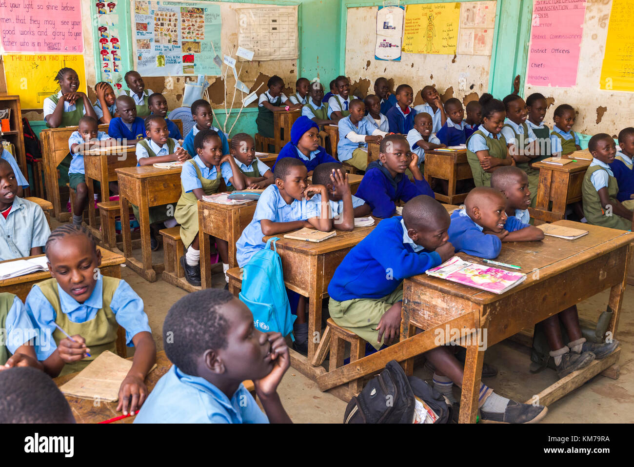 Schulkinder in Uniform saßen an Holztischen und hörten während des Unterrichts ihrem Lehrer in Nairobi, Kenia, zu Stockfoto