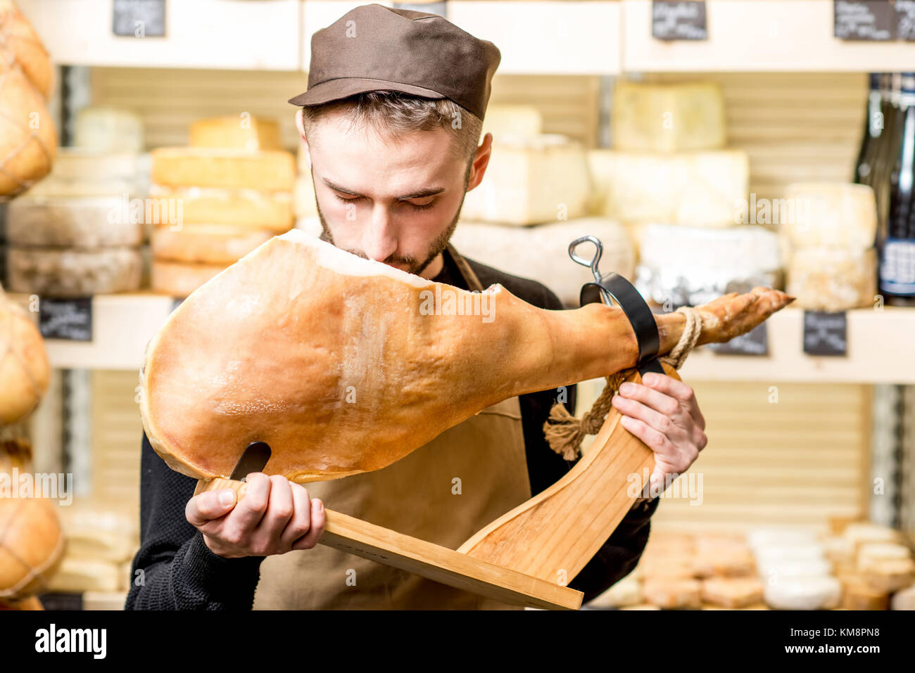 Portrait einer jungen Contador mit Prosciutto Bein stehend vor dem Store Schaufenster voller Käse Stockfoto