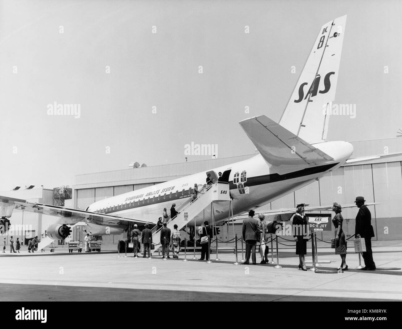 Die SAS DC-8-33, ein Verkehrsflugzeug aus den 1960er Jahren, wurde während des Bodens am Boden gezeigt. Passagiere steigen sowohl von der Vorder- als auch von der Rückseite des Flugzeugs ein, wobei die frühen Praktiken des Bodendienstes hervorgehoben werden. Stockfoto