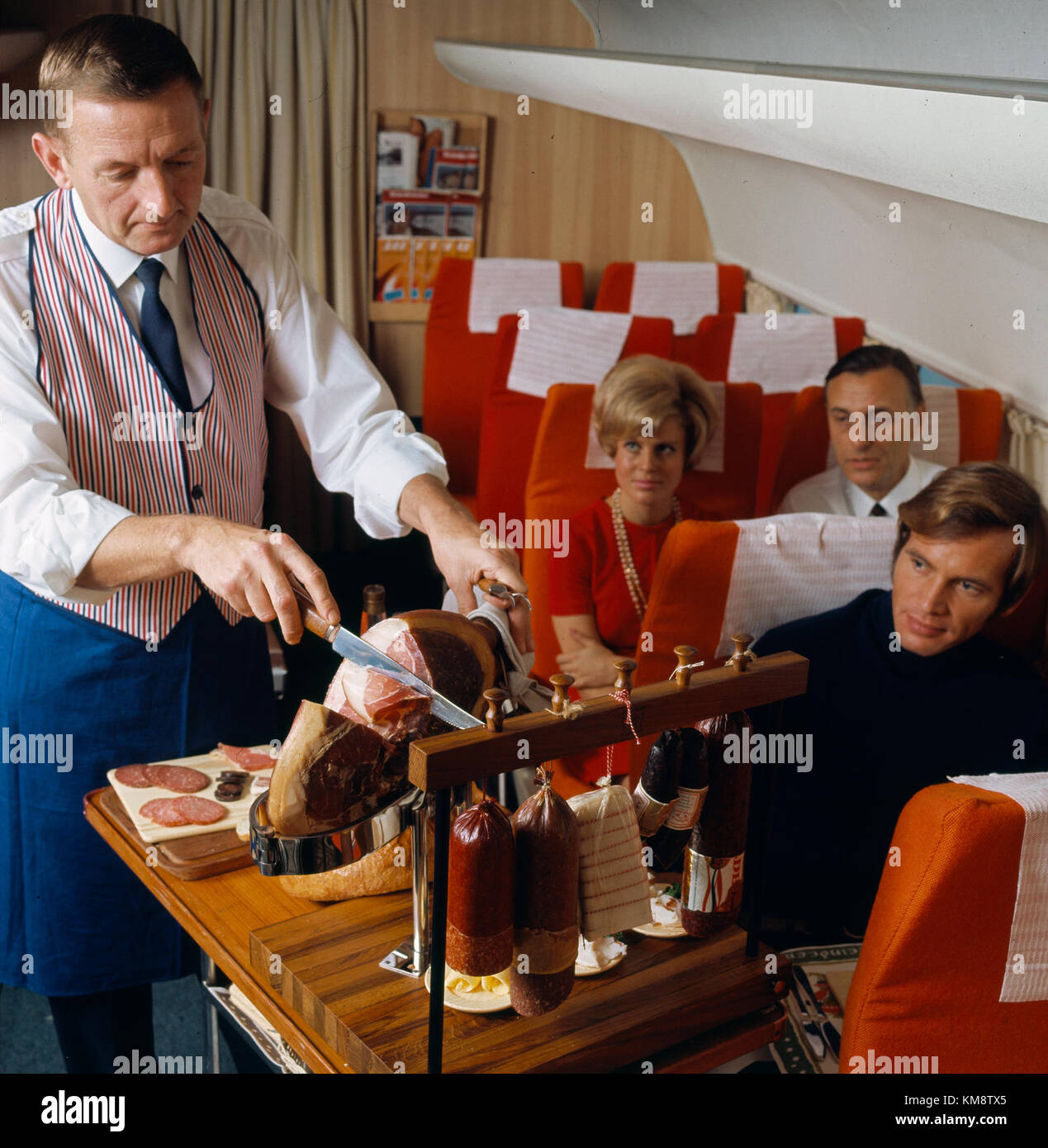 Dieses Bild zeigt das Innere eines Scandinavian Airlines System (SAS) DC-8-Flugzeugs und zeigt den Bordservice, bei dem ein Steward den Passagieren ein skandinavisches Buffet im Landhausstil serviert. Stockfoto